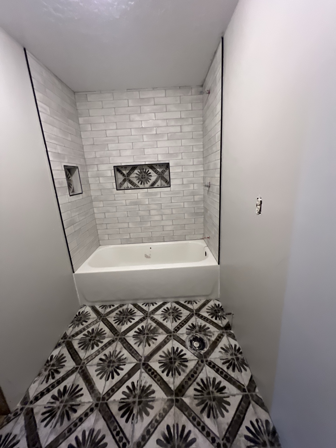 White tile tub surround with niches and patterned floor during installation