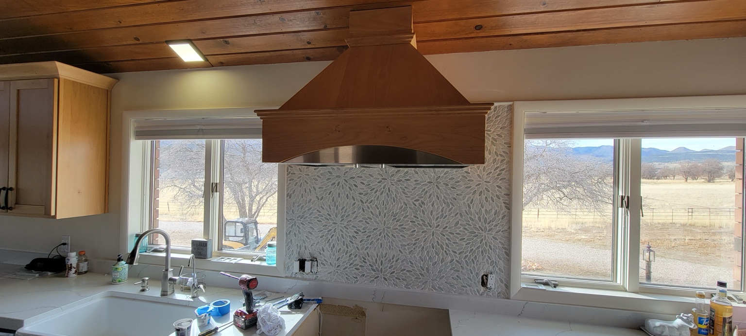 Decorative mosaic backsplash beneath a wood range hood